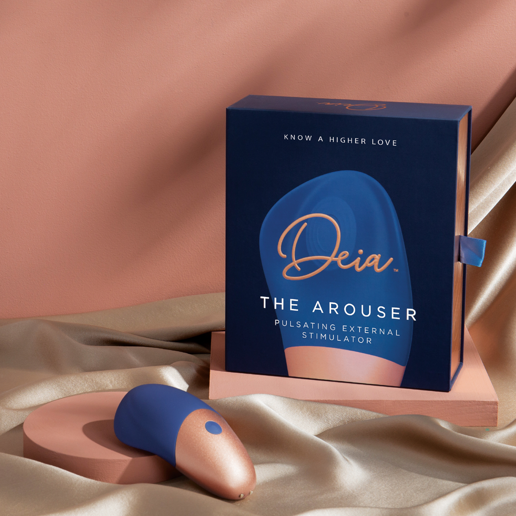 Deia's AROUSER pulsating clitoral stimulator shown with gift box and out of box product on silk cloth